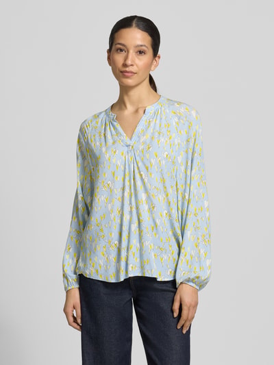 Frauenmodel trägt Regular Fit Bluse aus reiner Viskose mit Allover-Motiv-Print von Emily Van den Bergh, hellblau-gelb, elastische Ärmelabschlüsse, Tunika-Ausschnitt, Langärmelig, Rückenlänge 68 cm bei Größe 36, Ärmellänge 65 cm, Ganzkörperansicht von vorne.