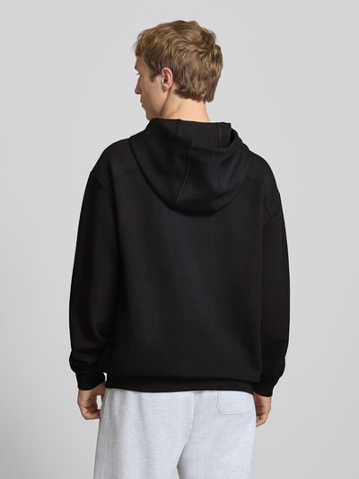Männermodel trägt Hoodie mit Logo von PUMA PERFORMANCE in Schwarz, Relaxed Fit, Material-Mix mit Lyocell, Ganzkörperansicht Rückansicht.