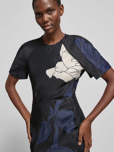 Frauenmodel trägt Slim Fit Maxikleid aus reiner Viskose von Victoria Beckham mit floraler Allover-Print, Rundhalsausschnitt, Kurzärmelig, dunkle Blau- und Cremetöne, glatte Textur, Nahaufnahme Oberkörper. Gesamtlänge 142 cm, Brustweite 40 cm, Ärmellänge 27 cm.