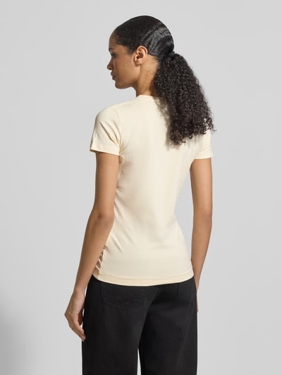 Vrouwenmodel draagt Slim Fit T-shirt met Ziersteinbesatz van Guess in licht beige katoenmix met logodetail, ronde hals, ruglengte maat S 62 cm. Ganzecoörperaanzicht achteraan.
