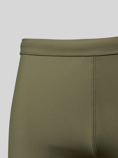 Männermodel trägt Slim Fit Bade-Trunks mit Logo-Detail von Calvin Klein Underwear, olivgrün, glatte Textur, Nahaufnahme Oberkörper.