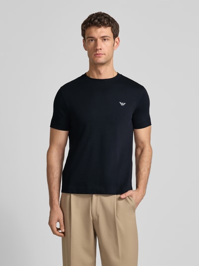 Männermodel trägt T-Shirt mit Label-Stitching und Rundhalsausschnitt von Emporio Armani in Schwarz, Slim Fit, reine Baumwolle, Nahaufnahme Oberkörper.