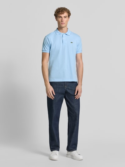 Männermodel trägt Regular Fit Poloshirt aus reiner Baumwolle von Lacoste in Hellblau, kombiniert mit Jeans, Ganzkörperansicht von vorne. Herren Poloshirt von Lacoste.