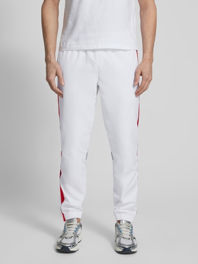 Männermodel trägt Regular Fit Trainingsanzug mit Kontraststreifen von Lacoste Sport in Weiß mit roten Streifen, elastischen Bündchen, Nahaufnahme Unterkörper.