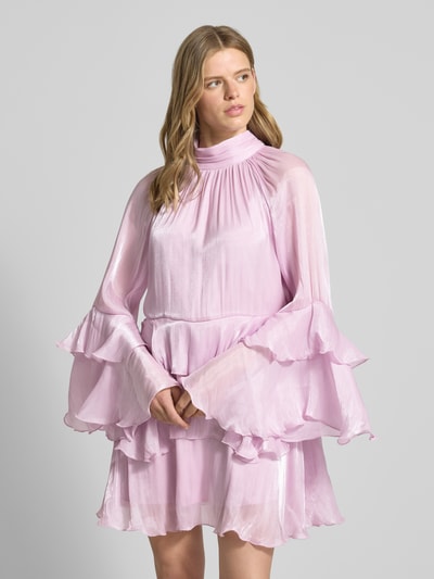 Frauenmodel trägt Minikleid im Stufen-Look Modell 'Flowy frill' von Gina Tricot in zartem Rosa mit Stehkragen, Volants und Rückenschnürung, A-Linie, ganz leichte Textur, Nahaufnahme Oberkörper. Rückenlänge bei Größe 36: 91 cm, Brustweite 44 cm, Ärmellänge 61 cm.