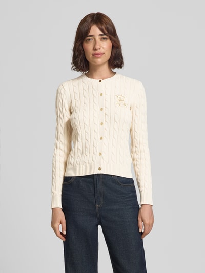 Frauenmodel trägt Regular Fit Strickjacke aus reiner Baumwolle Modell 'RALHAN' von Lauren Ralph Lauren in Creme mit Zopfmuster, Ganzkörperansicht von vorne.