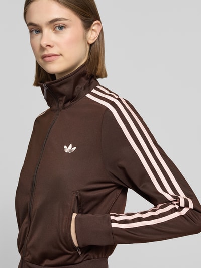 Frauenmodel trägt Regular Fit Sweatjacke mit Logo-Stitching von adidas Originals in Braun mit rosa Kontraststreifen, Nahaufnahme Oberkörper