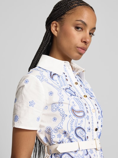 Frauenmodel trägt Hemdblusenkleid in Midilänge von Self-Portrait aus weißer Baumwolle mit blauen Paisley-Stickereien, tailliertem Schnitt, taillengürtel mit Dornschließe, Nahaufnahme Oberkörper.
