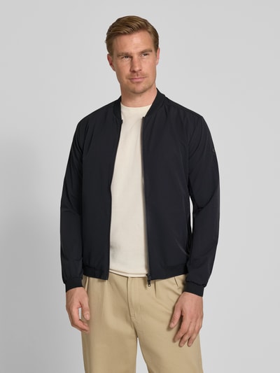 Männermodel trägt Regular Fit Jacke mit Stehkragen Modell 'Campo' von SCANDINAVIAN EDITION, Zweiwege-Reißverschluss, Eingrifftaschen, elastische Abschlüsse, schwarz, glatte Oberfläche, Ganzkörperansicht von vorne. Kontext: Rückenlänge bei Größe M: 67 cm, Schulterbreite: 44 cm, Brustweite: 51 cm, Ärmellänge: 64 cm.