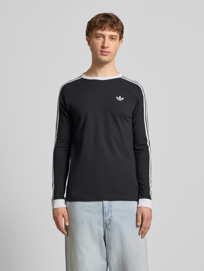 Männermodel trägt Longsleeve mit gerippten Abschlüssen von adidas Originals, schwarze Baumwolle, Regular-Fit, Label-Stitching, Ganzkörperansicht von vorne.