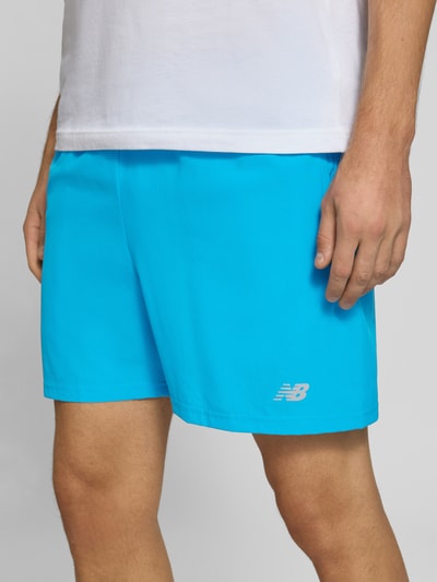 Männermodel trägt Shorts mit elastischem Bund und Logo von New Balance, leuchtend blau, Regular Fit, Nahaufnahme Oberkörper, Logo sichtbar.