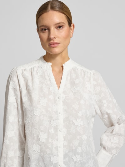 Kobiece model nosi Regular Fit Langarmbluse mit Baumwoll-Anteil od Tom Tailor, efekt: wzór na całej powierzchni, krój regular fit, kształt kołnierza: kołnierz z falbanami, kwiatowy wzór, dekolt w serek, listwa guzikowa, rękawy: długi rękaw, wykończenie materiału: popelina, kolor biały, tekstura delikatna, struktura lekko prześwitująca, kwiatowe hafty, widoczne guziki, Ganzkörperansicht z przodu