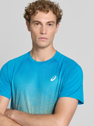 Męski model nosi t-shirt Regular Fit T-Shirt mit Logo-Print Model 'Road' von ASICS TIGER, niebieski z nadrukiem z logo, okrągły dekolt, długość tyłu w rozmiarze M: 70 cm, zbliżenie na górną część ciała