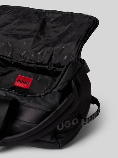 Produktfoto, czarna torba weekendowa Weekender mit Rucksackgurten model 'AYDEN_HOLDALL' od HUGO, z widoczną teksturą tkaniny i czerwonym logo, kontekst: torba weekendowa męska HUGO