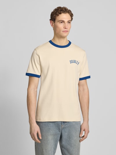 Męski model nosi T-Shirt mit Rundhalsausschnitt od Wood Wood, bawełna, krój regular fit, model 'Parker', paski w kontrastowym kolorze, długość tyłu w rozmiarze M: 71 cm, jasny beż z niebieskimi detalami, gładka faktura, całkowity widok z przodu.