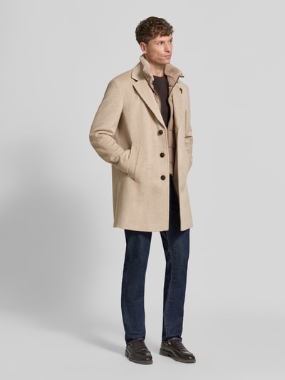 Männermodel trägt Regular Fit Mantel aus Woll-Mix Modell 'Morris' von JOOP! COLLECTION in Beige, kombiniert mit dunkler Hose, Ganzkörperansicht von vorne.