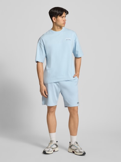 Männermodel trägt hellblaues T-Shirt mit Label-Detail von REVIEW aus reiner Baumwolle, lockerer Schnitt, Ganzkörperansicht von vorne.