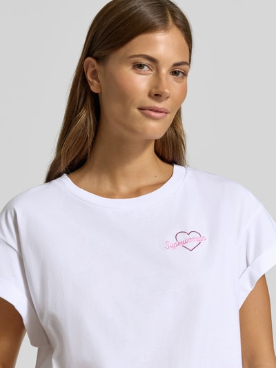 Frauenmodel trägt T-Shirt aus reiner Baumwolle von Rich & Royal in Weiß mit Statement-Stitching und fixierten Ärmelumschlägen, Nahaufnahme Oberkörper. Rückenlänge bei Größe S 60 cm, lockere Passform, überschnittene Schultern.