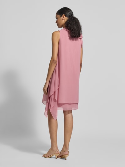 Modelka nosi Relaxed Fit Kleid mit Stehkragen od Vera Mont, różowy, półprzezroczysty, z ozdobną kokardą, długość tyłu w rozmiarze 36: 98 cm, szerokość w rozmiarze 36: 29 cm, widoczne nieprzezroczysta halka, widok całopostaciowy tyłem.