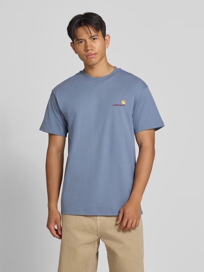 Męski model nosi Regular Fit T-Shirt aus reiner Baumwolle Modell 'American Script' von Carhartt Work In Progress, niebieski kolor, detal z logo, męski t-shirt, bawełna, krój regular fit, długość tyłu w rozmiarze M: 75 cm, Ganzkörperansicht von vorne.