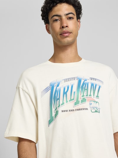 Männermodel trägt T-Shirt mit Label-Print Modell 'Sport Gradient' von KARL KANI in Creme mit großem bunten Frontprint, Nahaufnahme Oberkörper. Baumwolle, Boxy Fit, gerippter Rundhalsausschnitt.