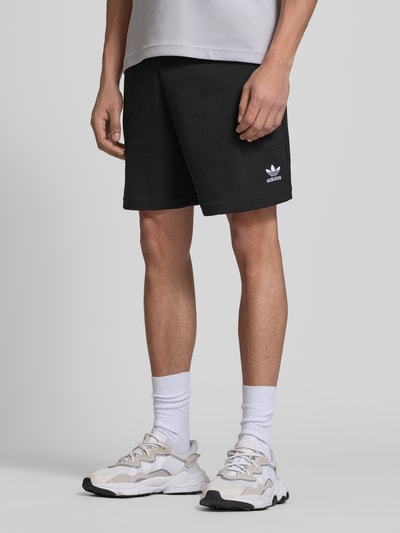Männermodel trägt Relaxed Fit Sweatshorts mit Baumwoll-Anteil von adidas Originals, schwarze Waffelstruktur, Logo-Stitching, Ganzkörperansicht von vorne.