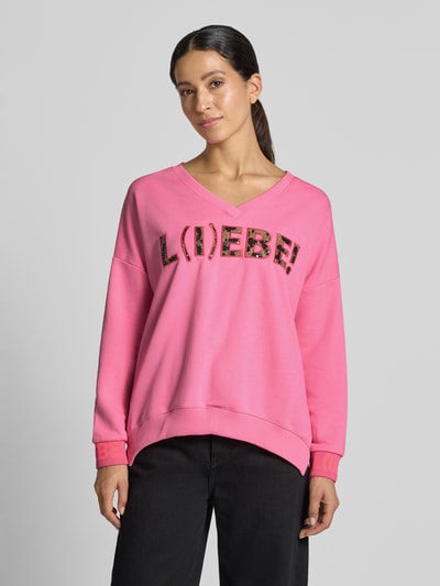 Vrouwenmodel draagt oversized dames sweatshirt van puur katoen, Model 'L(I)EBE' van miss goodlife, V-hals, met pailletten, statementprint, ribboordjes. Vooraanzicht bovenlichaam.