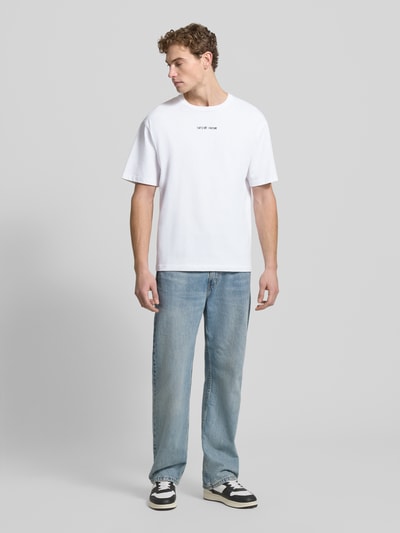 Männermodel trägt T-Shirt mit Label-Stitching von Samsøe Samsøe, Herren T-Shirt aus reiner Baumwolle, Regular-Fit, gerippter Rundhalsausschnitt, Rückenlänge bei Größe M 71 cm, weiße Farbe, Ganzkörperansicht von vorne.