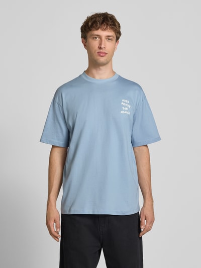 Männermodel trägt Herren T-Shirt von Only & Sons Modell 'MONEY' in Optik: Unifarben mit Statement-Print, Passform: Loose-Fit, Jersey aus reiner Baumwolle, Rundhals-Ausschnitt, Kurzarm, Ganzkörperansicht von vorne.