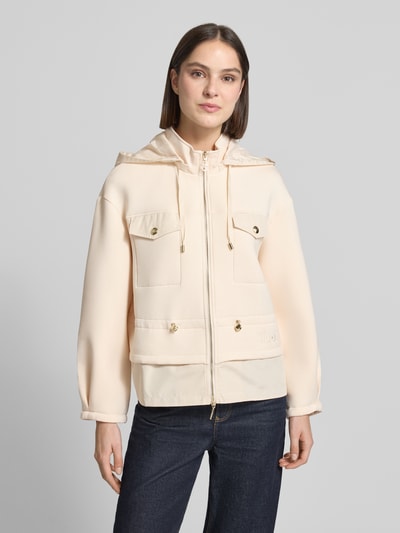 Frauenmodel trägt Jacke mit Pattentaschen und Kordelzug an der Taille von LIU JO SPORT, Viskose-Mix mit Stretch-Anteil, Beige, Gerader-Schnitt, Kapuze, Zweiwege-Reißverschluss, Logo-Stitching, Ganzkörperansicht von vorne.