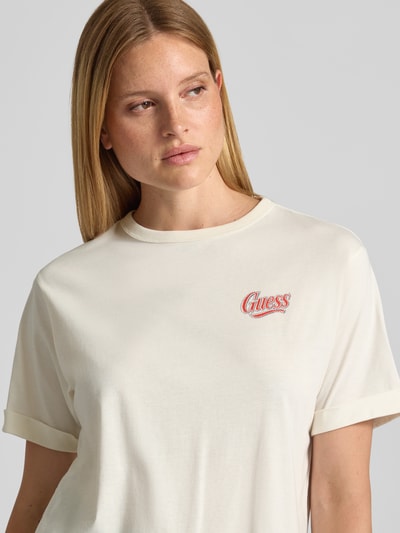Frauenmodel trägt Relaxed Fit T-Shirt mit Ziersteinbesatz Modell 'Emotional' von GUESS in Offwhite, Logo-Stitching, Nahaufnahme Oberkörper