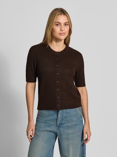 Modelka nosi Slim Fit Cardigan aus reinen Leinen in Strick-Optik od Stefanel, imitacja dzianiny, okrągły dekolt, listwa guzikowa, długość tyłu w rozmiarze S: 53 cm, długość rękawów w rozmiarze S: 29 cm, ciemnobrązowy, proste jeansy, ujęcie całej sylwetki od przodu.