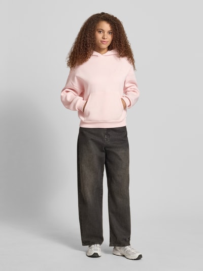 Vrouwenmodel draagt Hoodie met Logo-Print en Känguru-Tasche van REVIEW in lichtroze katoenmix, loose fit, capuchon, kangoeroezak, logoprint, ganzekörperaanzicht van voren.
