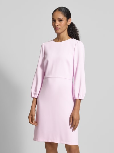 Modelka nosi Knielanges Kleid mit Rundhalsausschnitt und 3/4-Arm von Marc Cain, materiał z domieszką stretchu, prosty krój, długość do kolan, okrągły dekolt, rękawy 3/4, długość tyłu w rozmiarze 36: 95 cm, szerokość w rozmiarze 36: 43 cm, długość rękawa w rozmiarze 36: 53 cm, jasnoróżowy odcień, gładka tekstura, widok całej sylwetki z przodu.