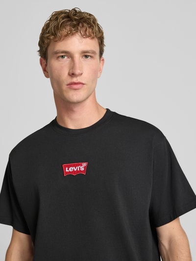 Mężczyzna model nosi Regular Fit T-Shirt aus reiner Baumwolle od Levi's®, czarny kolor z czerwonym logo, Nahaufnahme górnej części ciała.