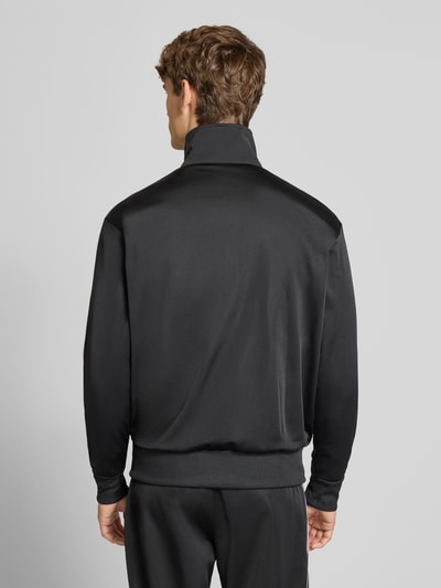 Männermodel trägt schwarze Sweatjacke mit Reißverschluss von adidas Originals, Stehkragen, gerippte Abschlüsse, Ganzkörperansicht Rückansicht.