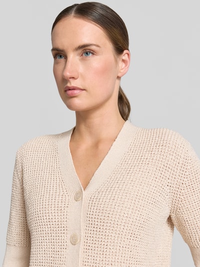Frauenmodel trägt Cardigan mit V-Ausschnitt Modell 'Temmy' von Someday in Beige, Material-Mix mit Baumwoll-Anteil, Knopfleiste, 1/2-Arm, Regular-Fit, Nahaufnahme Oberkörper.