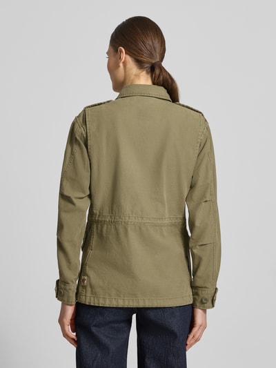 Modelka nosi kurtkę Regular Fit Jacke mit Umlegekragen Modell 'Buni' od khujo z bawełny, kolor oliwkowy, nakładane kieszenie, wyhaftowane logo, długość tyłu w rozmiarze S: 60 cm, szerokość ramion w rozmiarze S: 40 cm, szerokość klatki piersiowej w rozmiarze S: 50 cm, długość rękawów w rozmiarze S: 56 cm, widok całej sylwetki z tyłu.