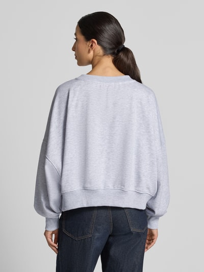 Frauenmodel trägt Oversized Sweatshirt mit Pailletten-Besatz Modell 'Amour' von miss goodlife aus Baumwolle, meliertes Hellgrau, elastische Abschlüsse, Ganzkörperansicht Rückansicht