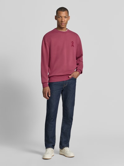 Männermodel trägt Relaxed Fit Sweatshirt aus reiner Baumwolle Modell 'ICONIC Å GMT' von ARMEDANGELS in Dunkelrot zu Jeans, Ganzkörperansicht von vorne.
