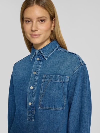 Vrouwenmodel draagt Oversized Jeanskleid uit lyocellmix van Armedangels in denimlook, borstzak, lange mouw, labelpatch, knoopsluiting, nahaufnahme bovenlichaam.