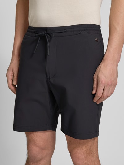 Mężczyzna nosi Straight Fit Shorts mit Eingrifftaschen Modell 'Drift' od SCANDINAVIAN EDITION, czarne, elastyczny materiał, z przodu, zbliżenie na górną część.