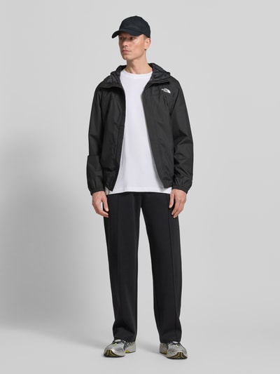 Männermodel trägt Jacke mit Kapuze von The North Face in Schwarz mit Label-Print, Regular-Fit, Reißverschlusstaschen, Ganzkörperansicht von vorne. Rückenlänge 76 cm, Schulterbreite 48 cm, Brustweite 68 cm, Ärmellänge 68 cm, verdeckter Reißverschluss.
