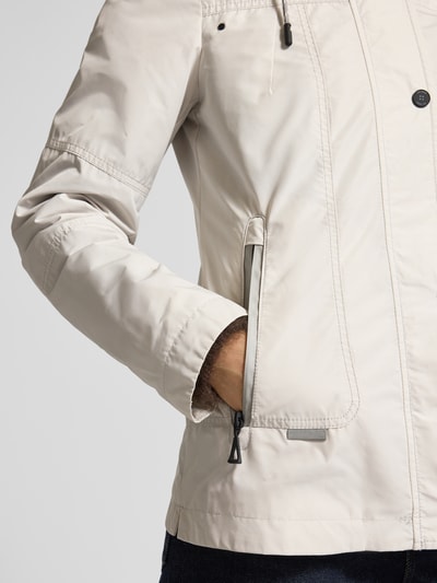 Frauenmodel trägt Weather Protection Jack mit Reißverschlusstaschen von Gil Bret in hellem Beige, glatte Textur, Nahaufnahme Oberkörper. Regular Fit, Kapuze mit Tunnelzug, Stehkragen und Reißverschlusstaschen erkennbar.