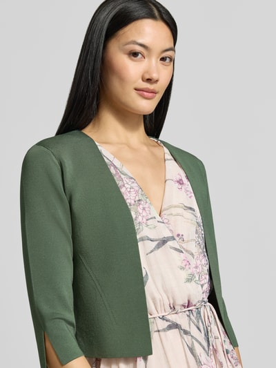 Frauenmodel trägt Regular Fit Bolero aus Viskose-Mix von Vera Mont in Dunkelgrün zu gemustertem Kleid, Nahaufnahme Oberkörper.