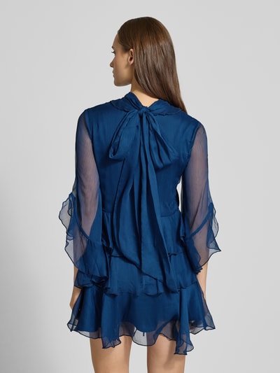 Frauenmodel trägt Cocktailkleid in Minilänge Modell 'NORAH' von Bardot aus blauem Chiffon mit Stufen-Look, 3/4-Ärmel, taillierte Passform, Stehkragen, Nahtreißverschluss, blickdichtem Unterrock und Taillenband, Ganzkörperansicht Rückansicht.