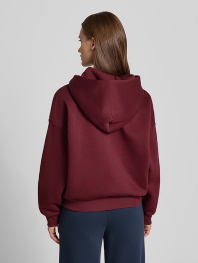 Modelka nosi Relaxed Fit Sweatjacke aus Baumwoll-Mix mit Label-Detail od REVIEW, ciemnoczerwony kolor, gładka tekstura, tył, widok całej sylwetki.