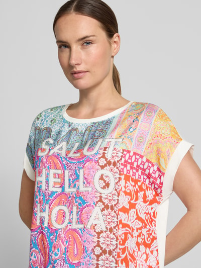 Frauenmodel trägt T-Shirt mit Viskose-Anteil von Milano Italy, bunte Muster, Ziersteine, Statement-Print, lockere Passform, Nahaufnahme Oberkörper.