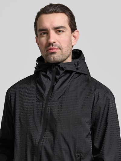 Männermodel trägt Jacke mit Zweiwege-Reißverschluss von Emporio Armani in Schwarz, strukturierte Oberfläche, Nahaufnahme Oberkörper. Regular Fit mit Kapuze, Reißverschlusstaschen, angeschnittener Schulter und dezenter Struktur.