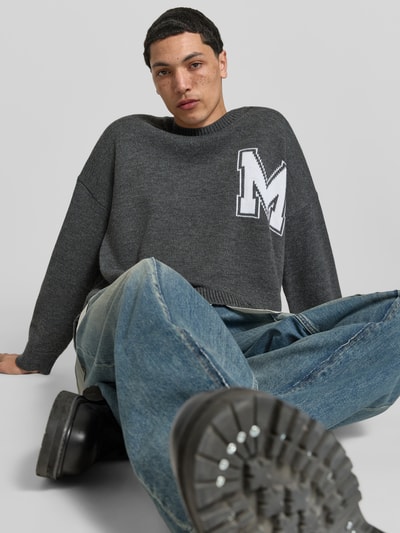 Männermodel trägt Oversized Pullover aus Woll-Mix von MM6 Maison Margiela, Strick-Optik, Logo-Stitching, Rundhalsausschnitt, Rückenlänge 80 cm, Ganzkörperansicht von vorne.